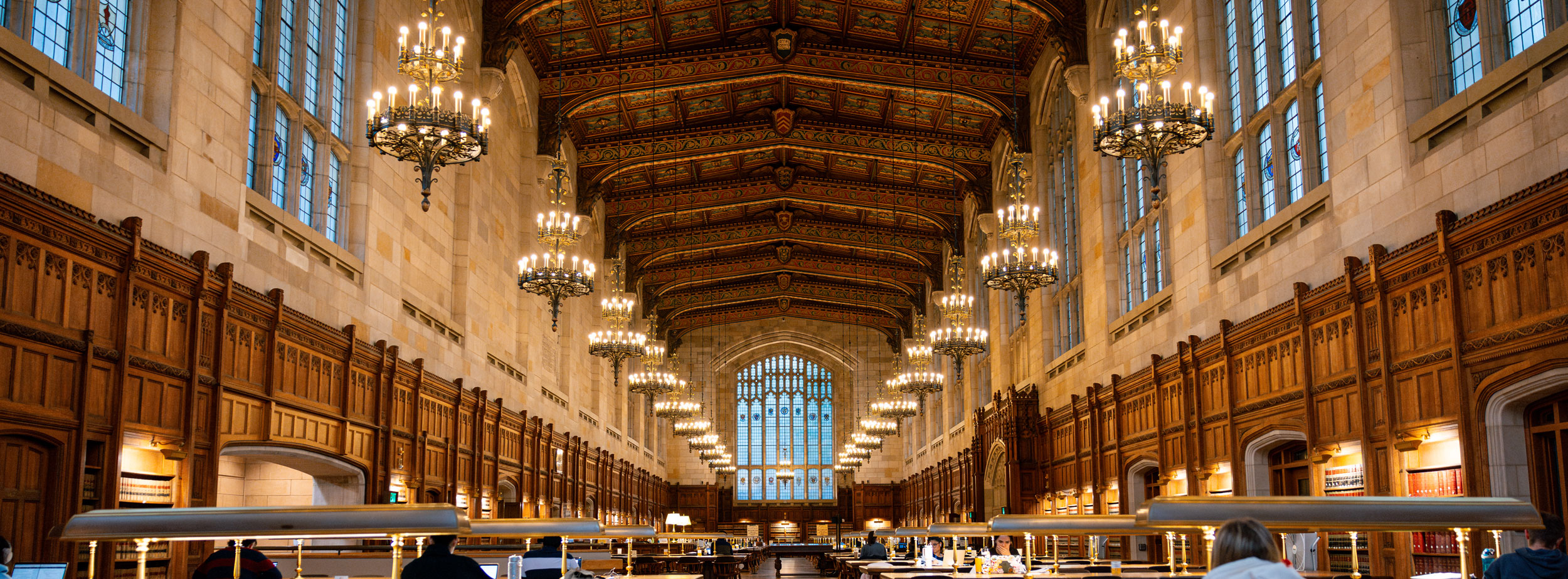 Students study at the tables singing the sides of the Law Library’s reading room. The candelabra-inspired lighting fixtures and tall stained glass windows fill the space with a warm glow.