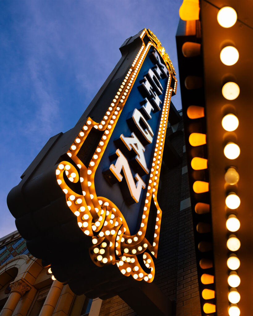 The lights on the Michigan Theater sign at sunset, catching golden highlights from the last rays of daylight, set against a dark blue sky with wispy pink clouds